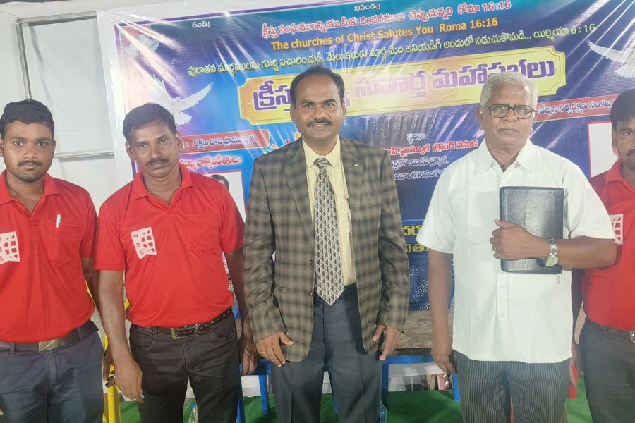 Standing with brethren at a gospel meeting banner